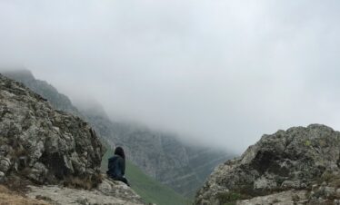 man in blue jacket sitting on rock mountain during daytime