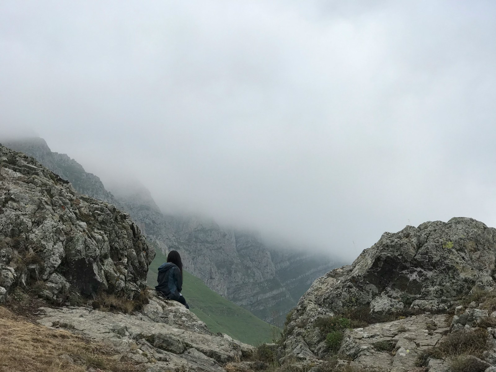 man in blue jacket sitting on rock mountain during daytime